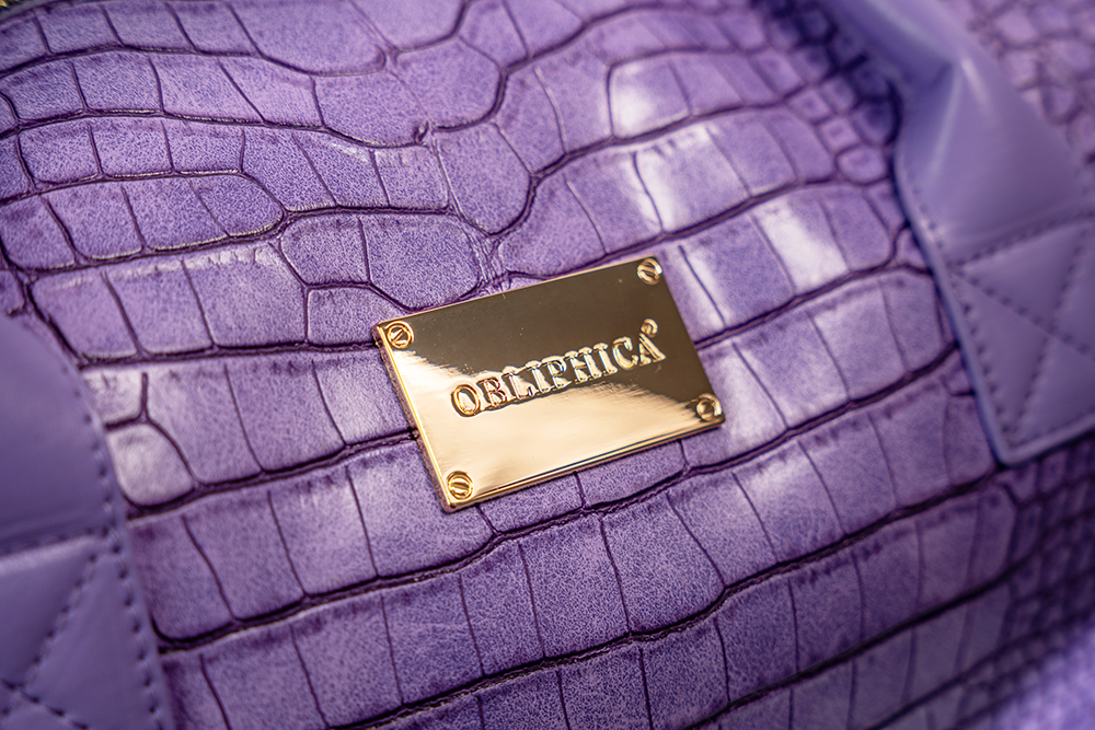 Purple textured handbag with a gold logo tag featuring the brand name.