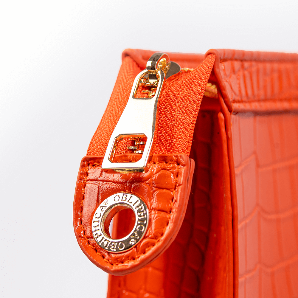 Close-up of a red handbag with a gold zipper pull on a white background